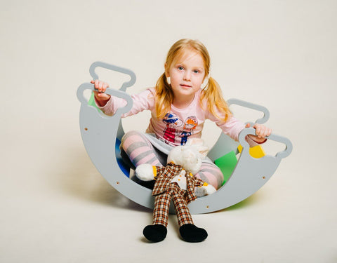 1. Child sitting inside colorful rainbow climber holding a toy