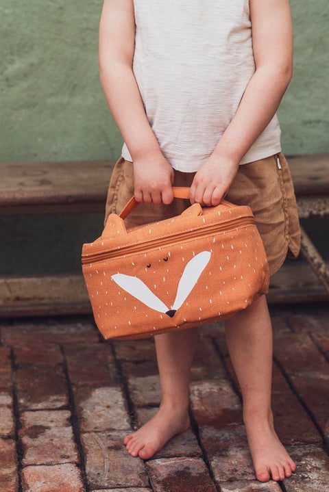 1. Child holding Trixie Baby Mr. Fox thermal lunch bag with playful fox design, standing on brick floor