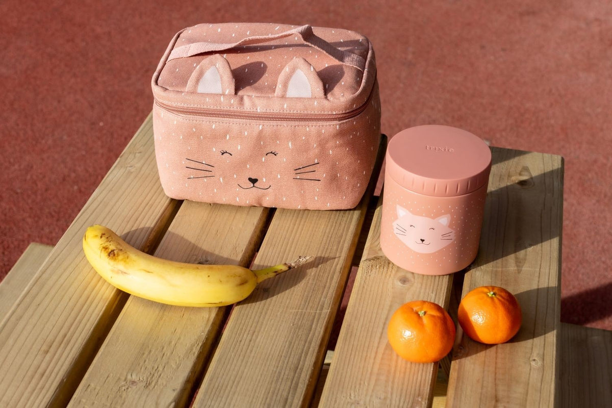 2. Trixie Baby Mrs. Cat thermal lunch bag with cat face design on wooden bench, next to banana and oranges