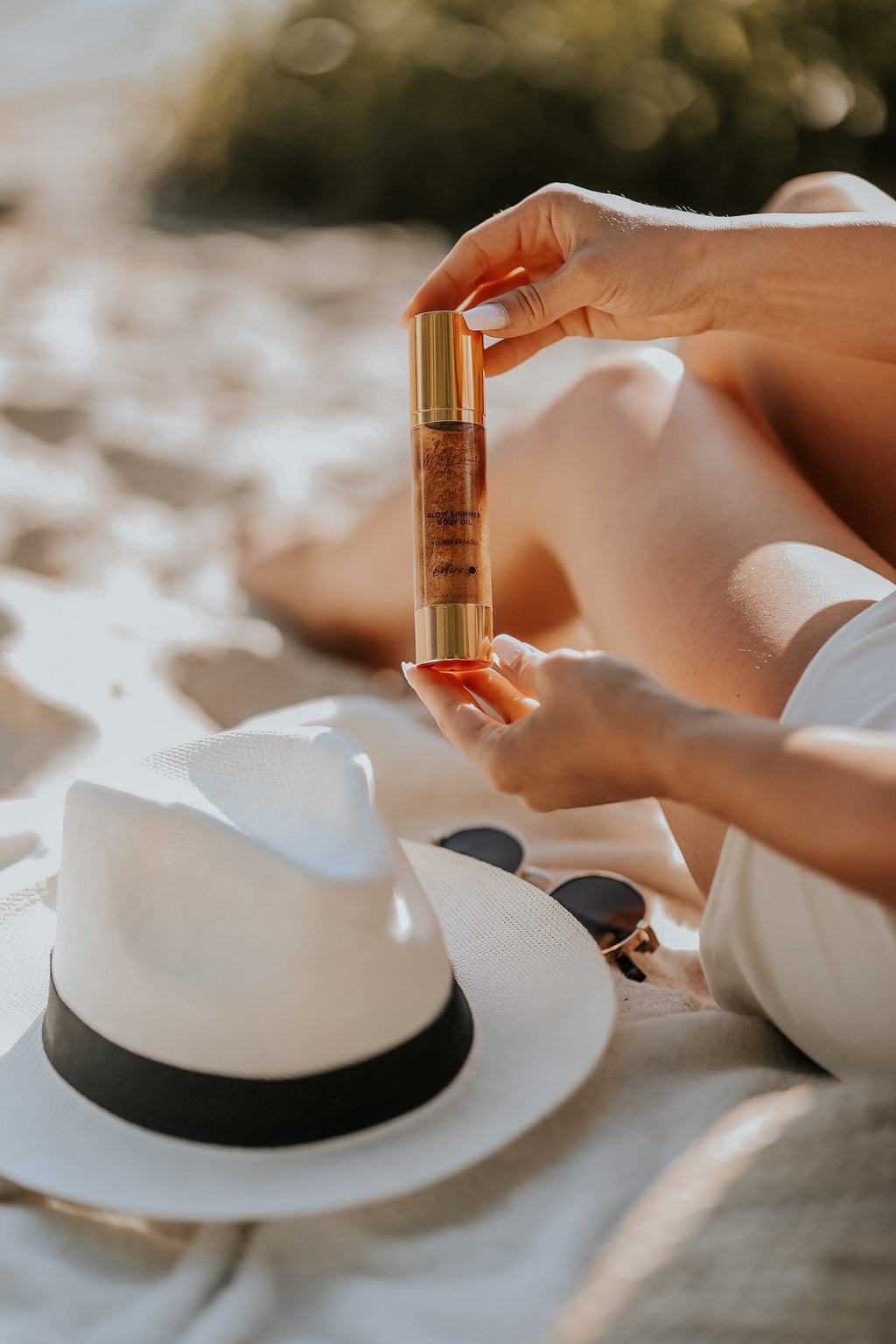 1. Woman holding North Beauty Tinted Glow Oil on a sandy beach, showcasing sun-kissed glow effect