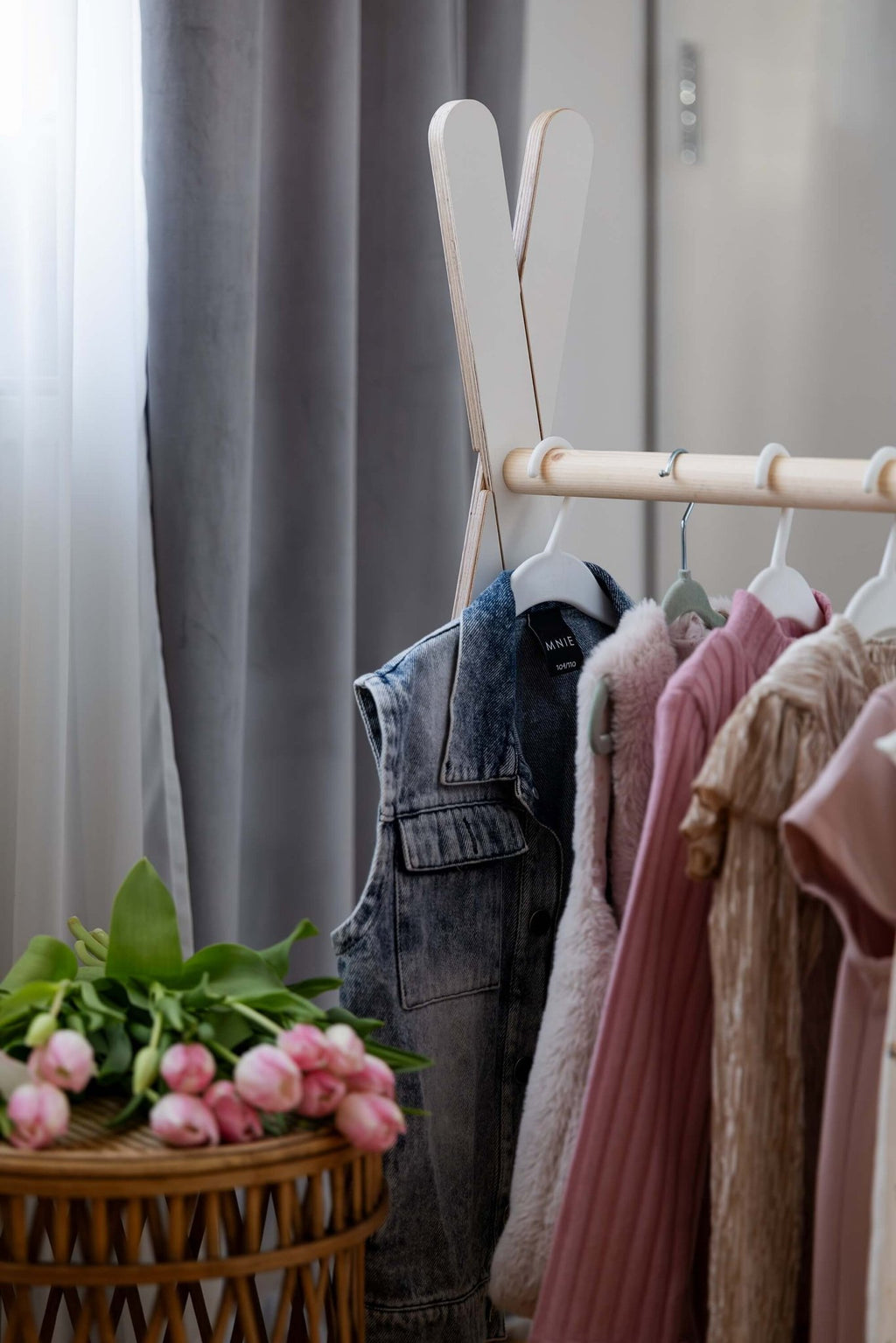 3. Close-up of MeowBaby Tipi clothing rack with children's clothes hanging, next to a wicker basket with pink flowers