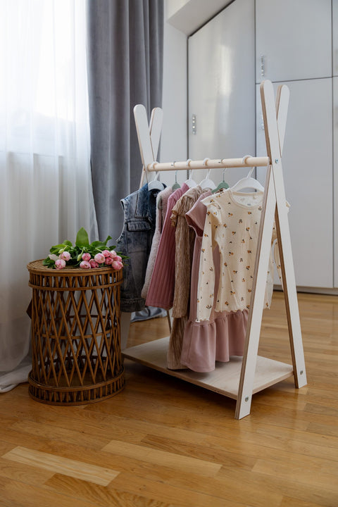 1. Children's white Tipi clothing rack by MeowBaby in a room setting with dresses and a wicker basket with flowers