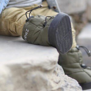1. Child wearing Stonz toddler puffer booties in cypress green sitting on stone steps outdoors