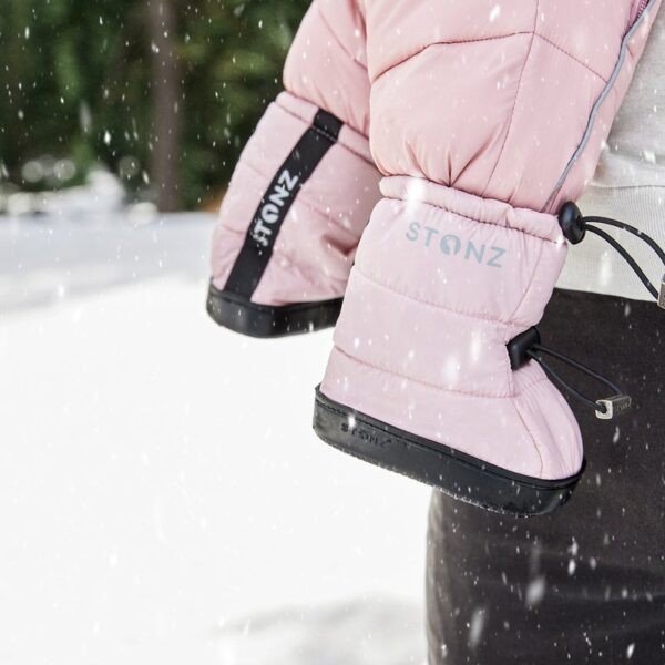 1. Toddler wearing Stonz haze pink puffer booties with black soles in snowy outdoor setting