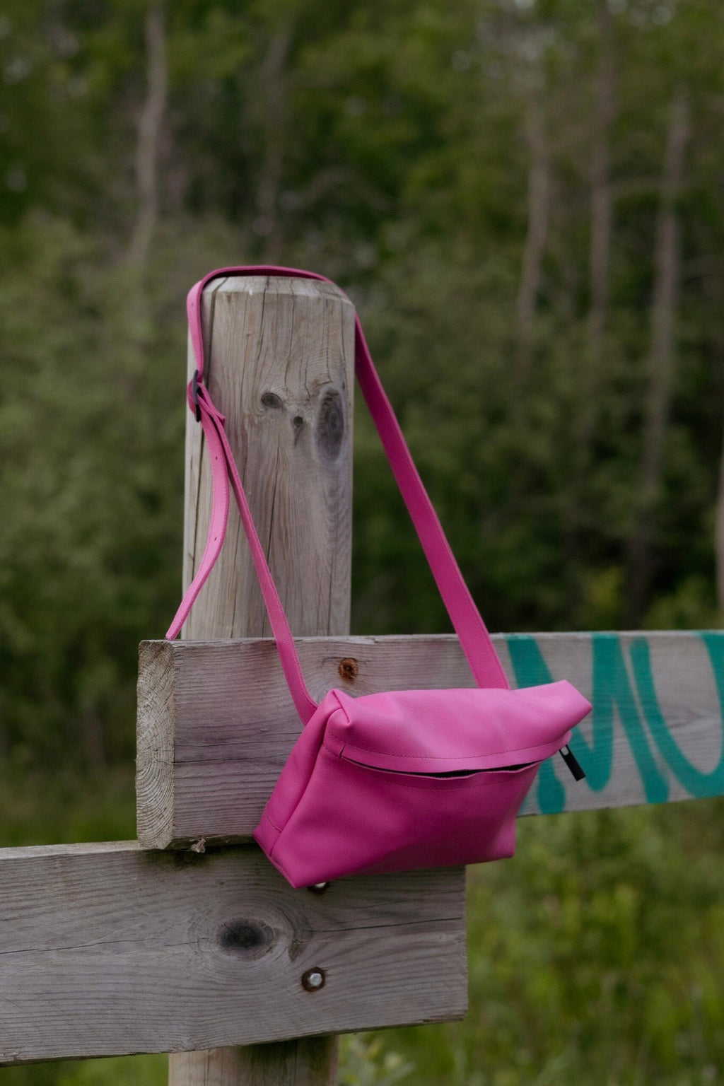 2. Omaking TOKU Lisbon pink leather bag hanging on a wooden fence in a natural setting