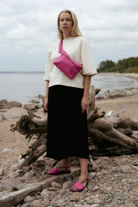 1. Woman wearing Omaking TOKU Lisbon pink leather bag across her shoulder on a beach
