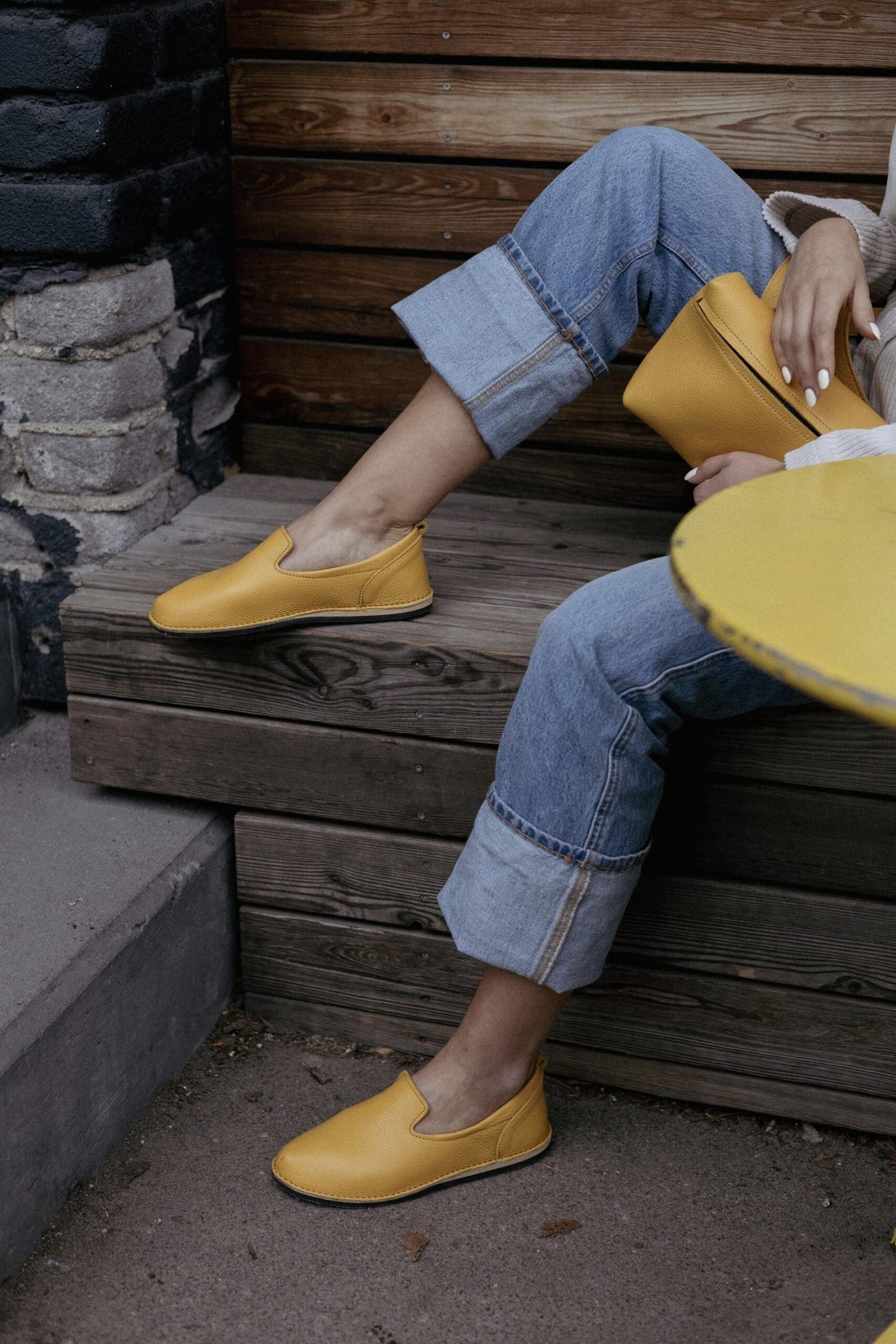 1. Woman holding yellow TOKU Lisbon bag by Omaking, styled with matching shoes, sitting on wooden steps