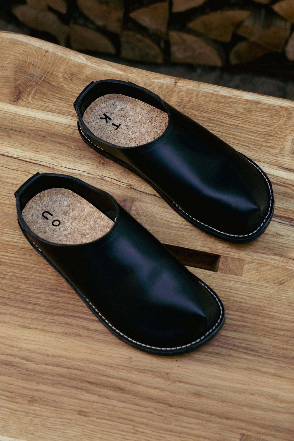 4. Flat lay of unisex black slip-on shoes with cork insoles on wooden surface, showcasing minimalist design