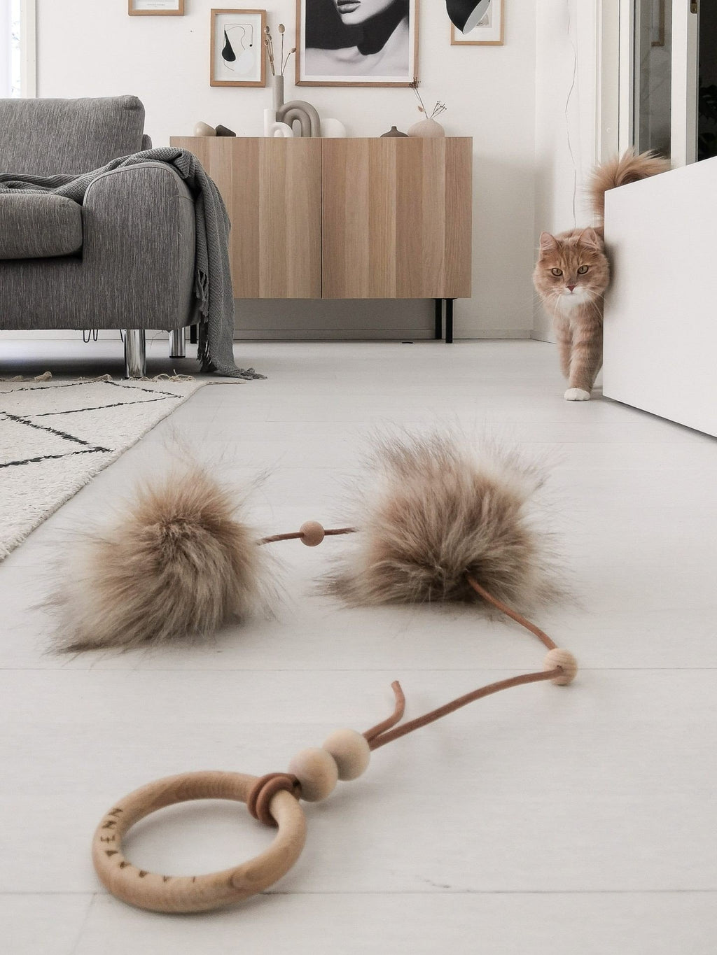 1. Cat approaching Labbvenn Tollo cat toy with faux fur balls on a light wooden floor in a stylish room