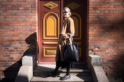 1. Woman in brown coat standing on steps with black Stella Soomlais tote bag in front of ornate door