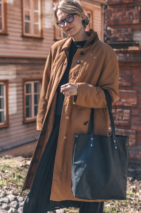 1. Woman in brown coat holding black Stella Soomlais tote bag outdoors near brick building