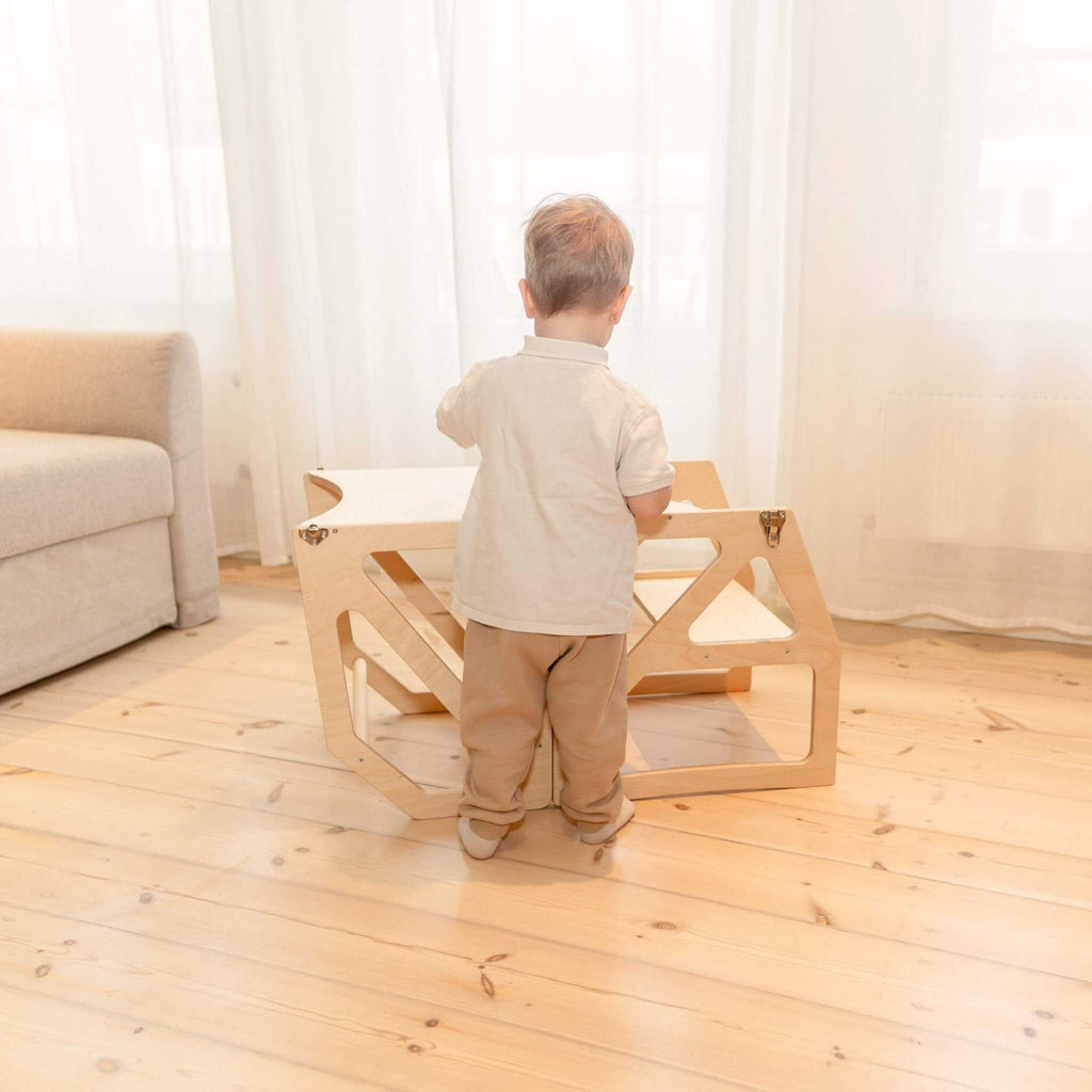 1. Toddler standing next to natural birch kitchen tower folded into table and chair in living room