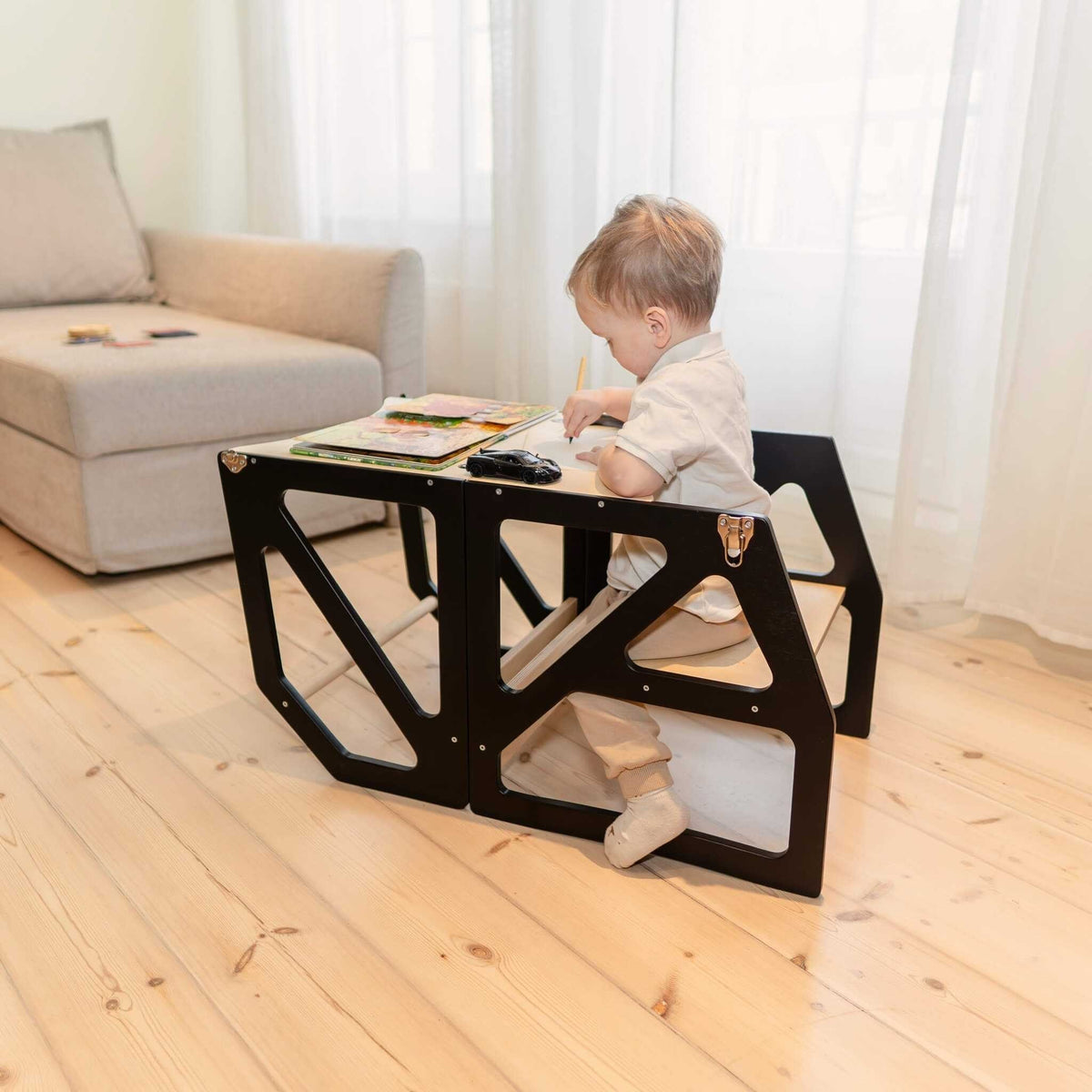 1. Toddler sitting at black transformable kitchen tower used as table and chair in living room