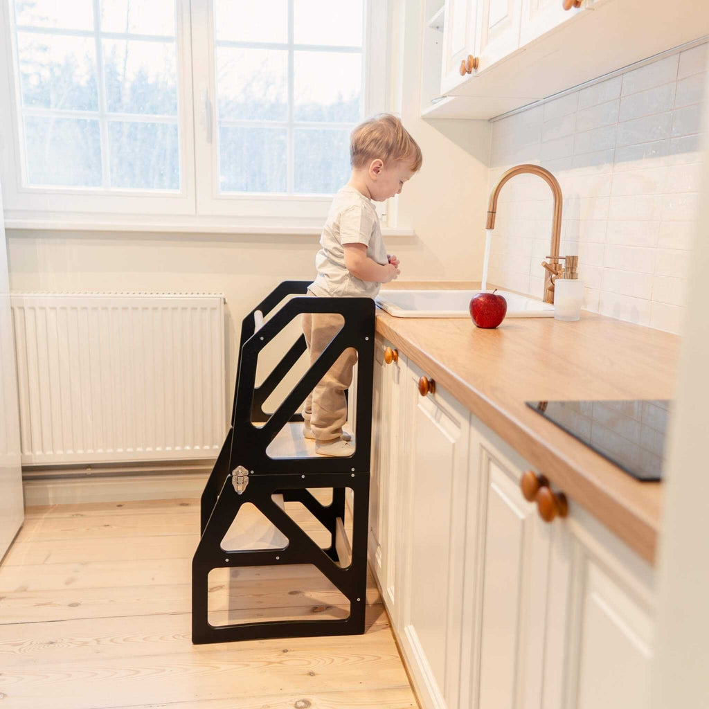 1. Toddler using black kitchen tower at sink in bright kitchen