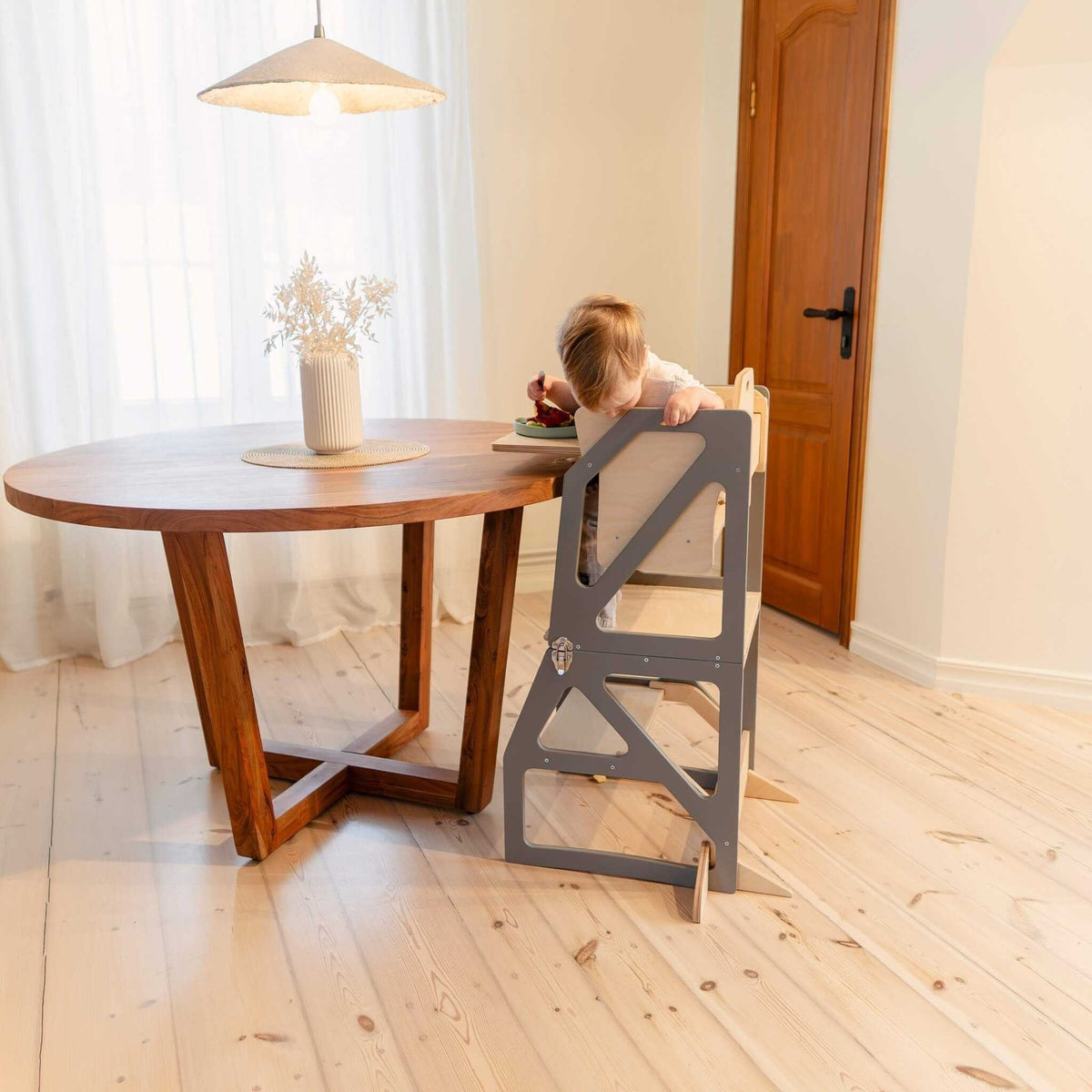 1. Child using gray transformable kitchen tower as a high chair at dining table