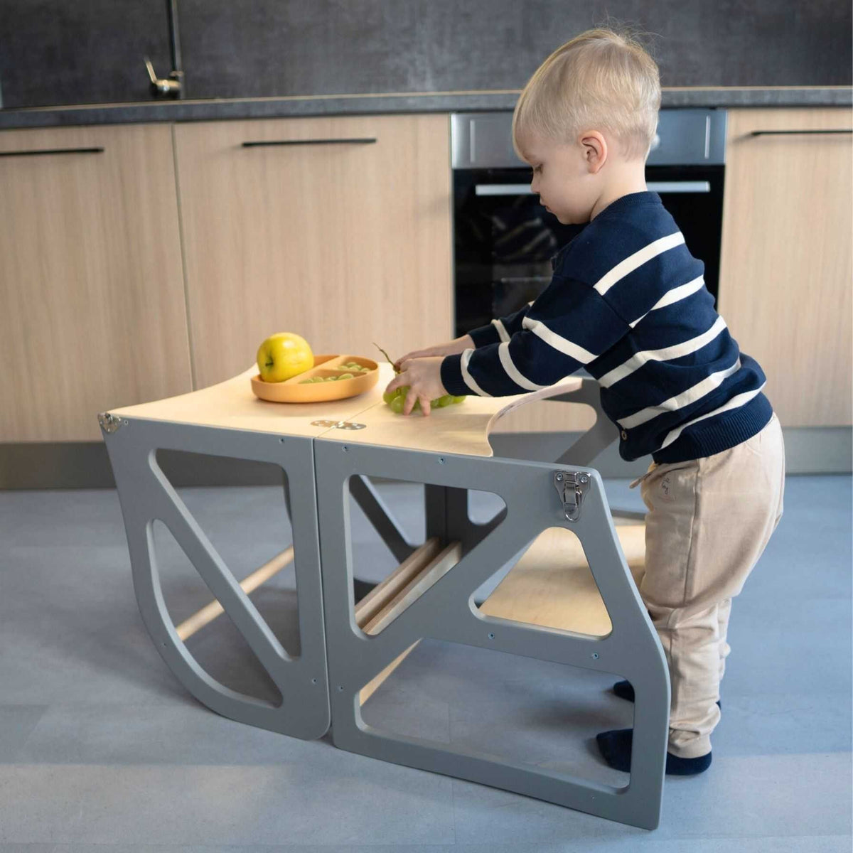 1. Child using gray transformable kitchen tower as a table in a kitchen, cutting fruit