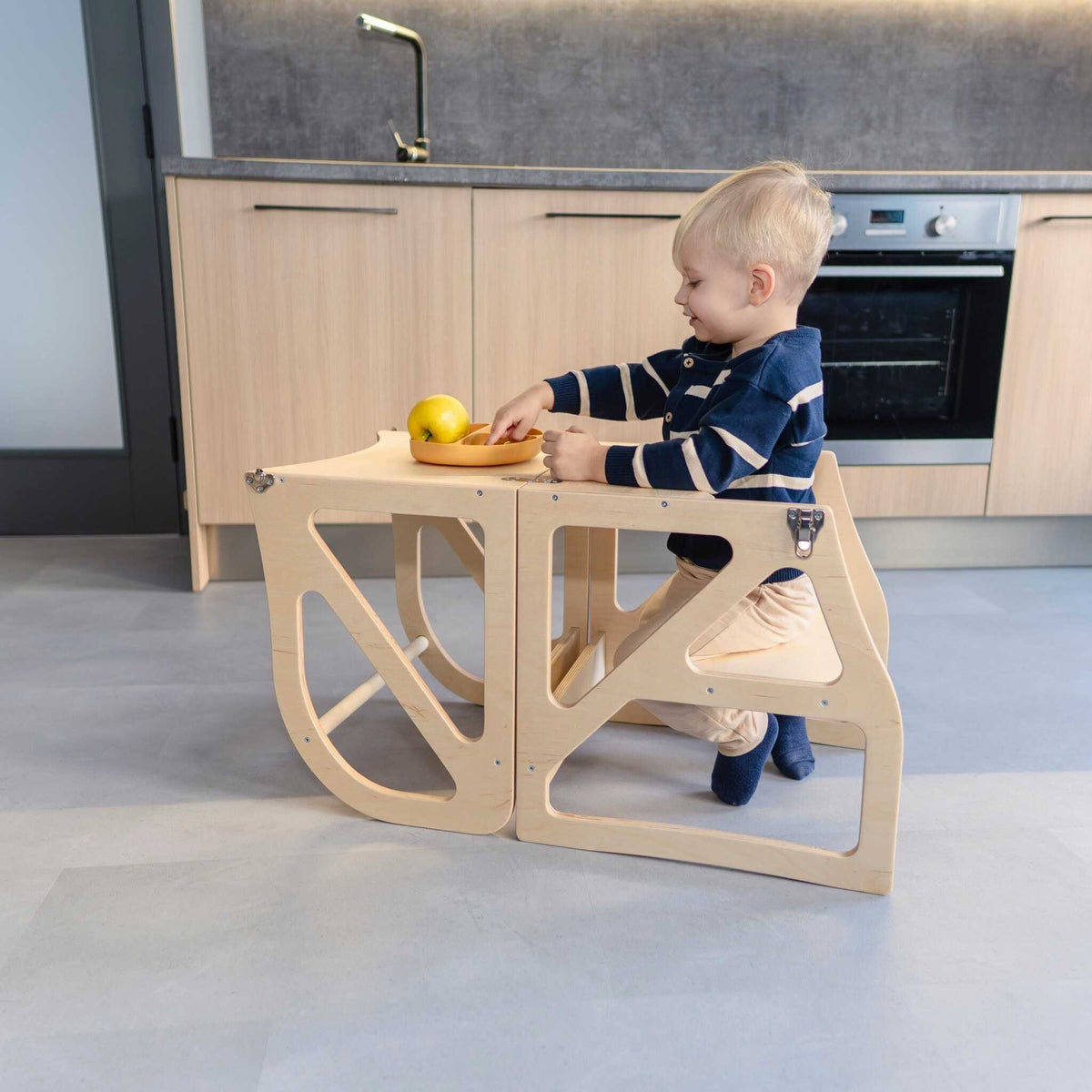 1. Child sitting at natural birch plywood transformable kitchen tower used as a table in a kitchen