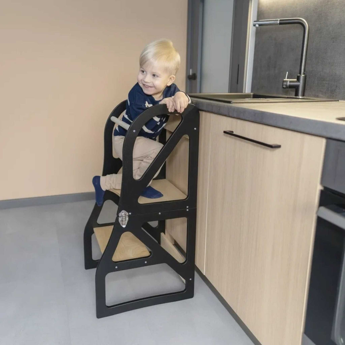 1. Child climbing black transformable kitchen tower next to a kitchen counter