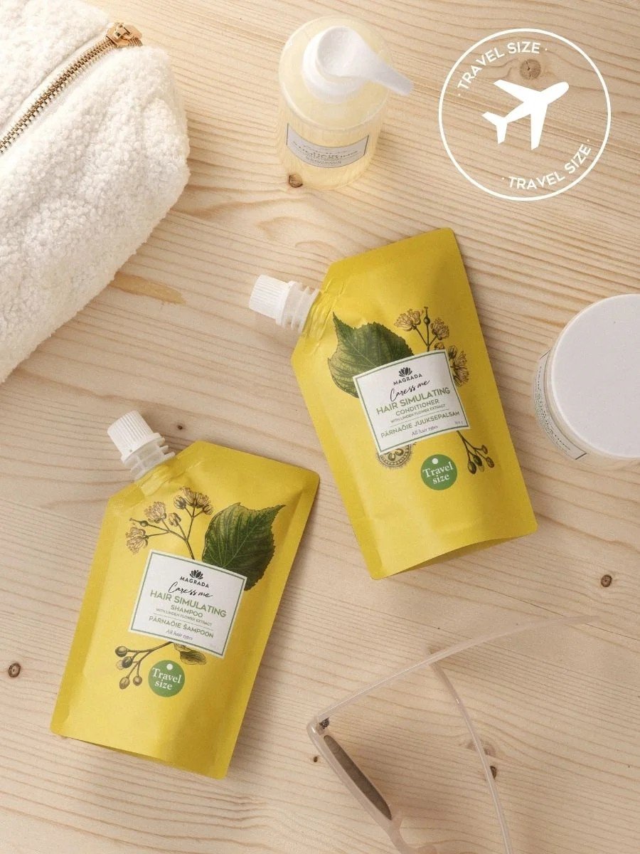 2. Flat lay of two travel size Magrada Organic Cosmetics linden flower conditioners on wooden surface with travel essentials
