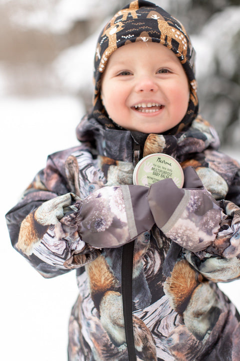 1. Happy child in animal print winter outfit holding Nurme baby balm in snowy environment