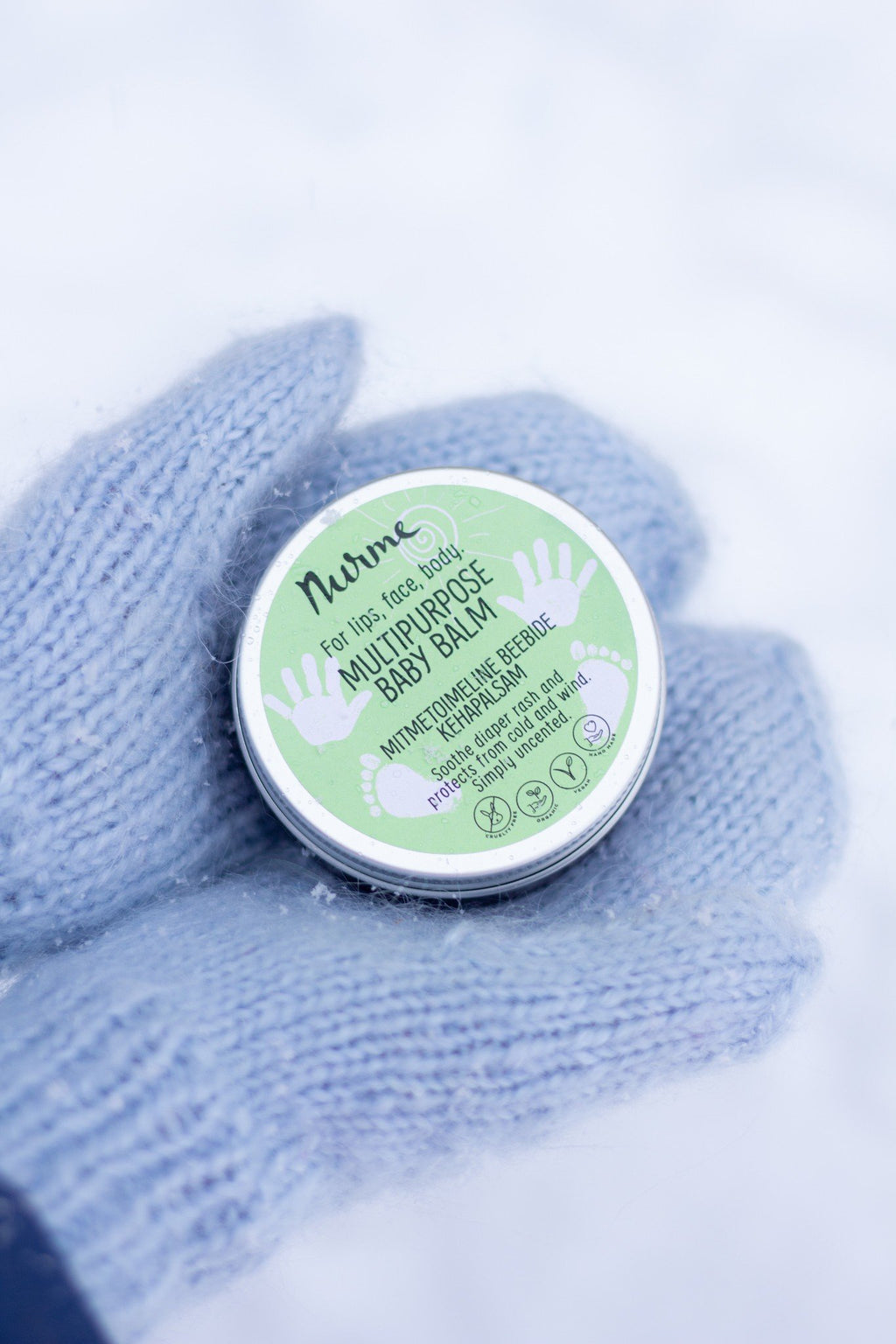3. Close-up of Nurme baby balm held in blue-gloved hand against snow background