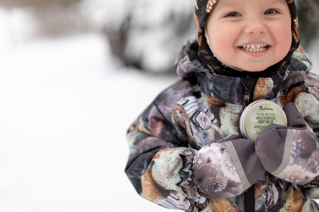 1. Smiling child in winter clothing holding Nurme multipurpose baby balm in snowy outdoor setting