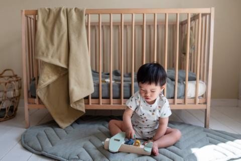 4. Child sitting on floor in nursery playing with Trixie Baby wooden xylophone, crib in background