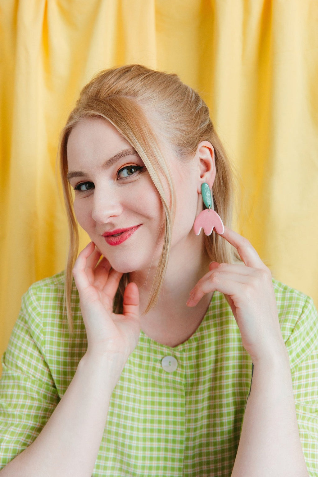 1. Woman wearing Rozenthal Porcelain Tulip Earrings with pink and green design, styled with a green checkered dress, against a yellow background