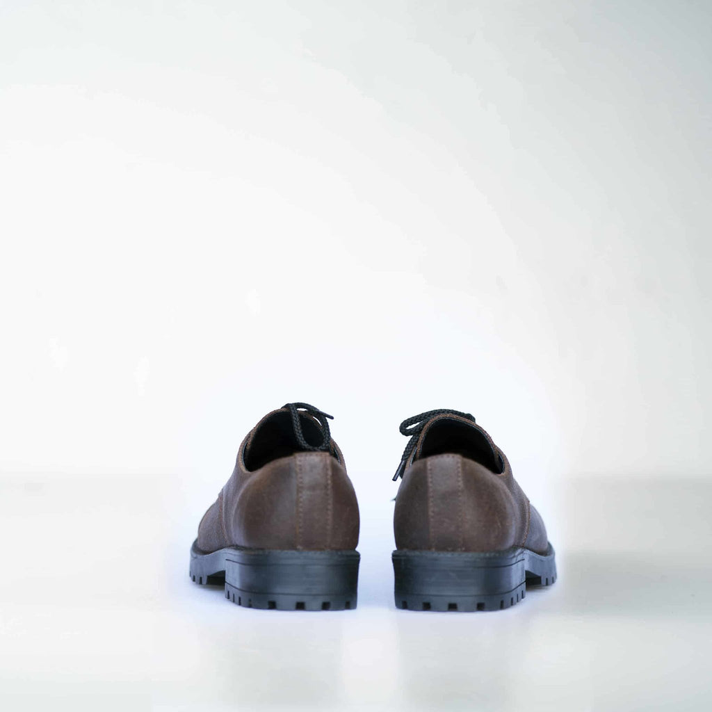 3. Back view of unisex dark brown Samelin Widgets shoes, highlighting sturdy construction, studio setting