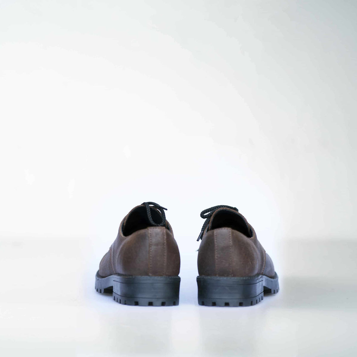 3. Back view of unisex dark brown Samelin Widgets shoes, highlighting sturdy construction, studio setting