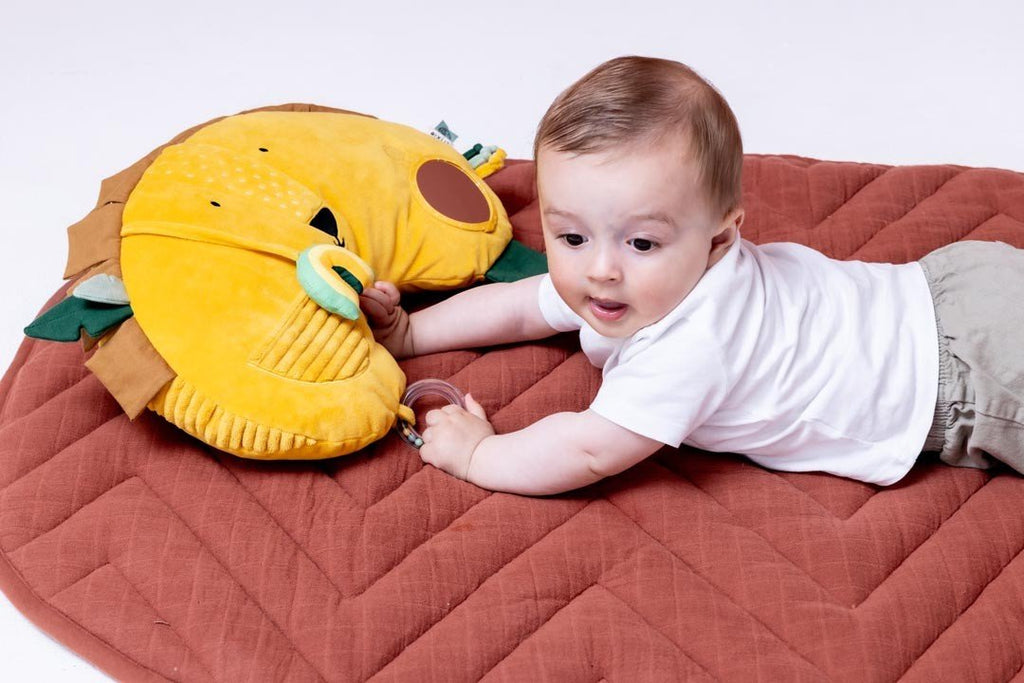 1. Baby lying on tummy on a brown mat, interacting with Trixie Baby's Mr. Lion tummy time pillow, featuring sensory elements and a lion face design