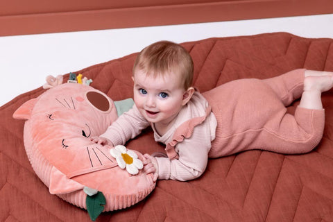 4. Smiling baby playing with pink Trixie Baby tummy time pillow with cat design, featuring sensory elements, on a quilted mat