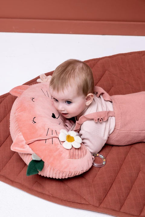 1. Baby lying on pink Trixie Baby tummy time pillow with cat design, featuring sensory elements like a flower and leaf, on a quilted mat
