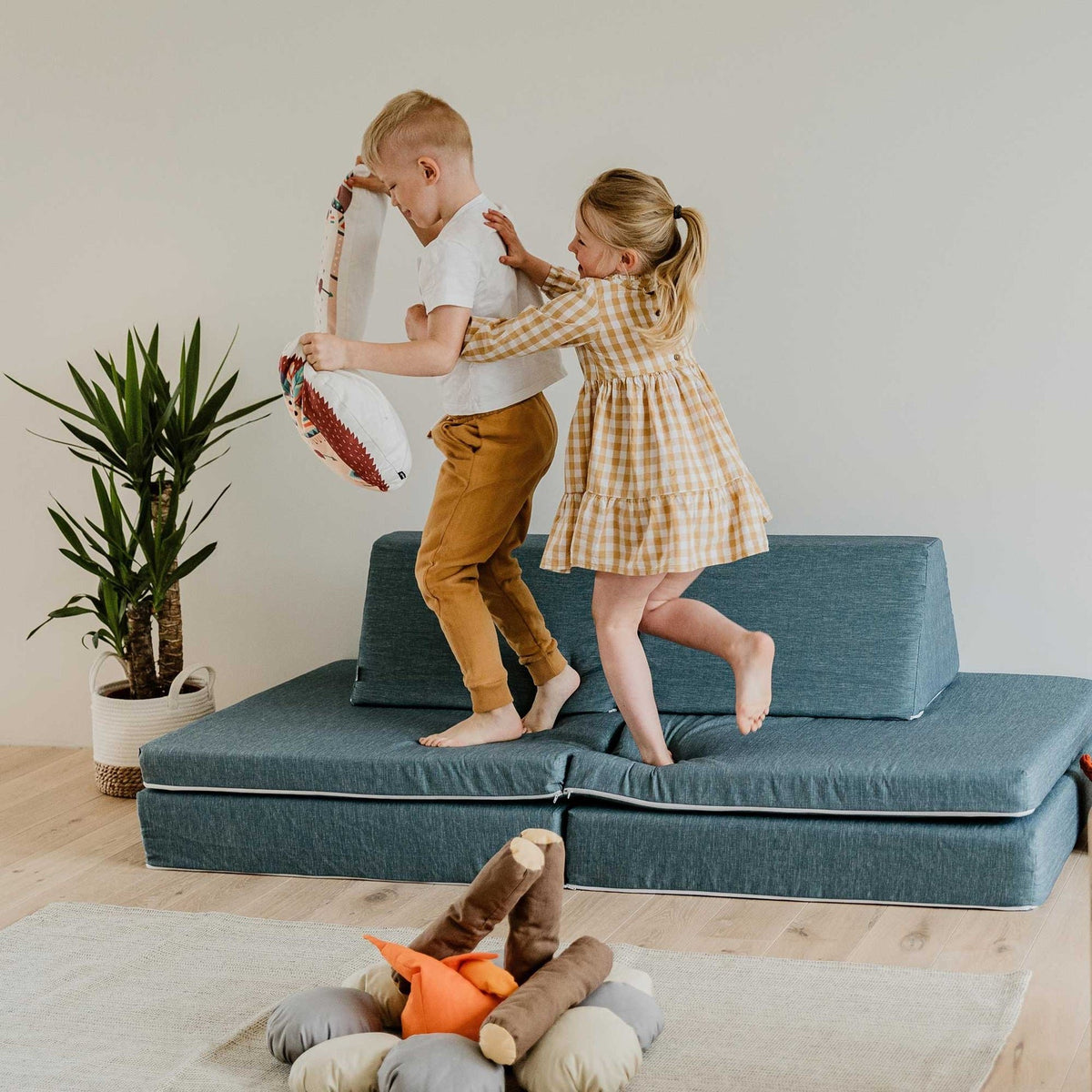 3. Two children playing on turquoise Monboxy play mattress sofa in a bright room with a plant
