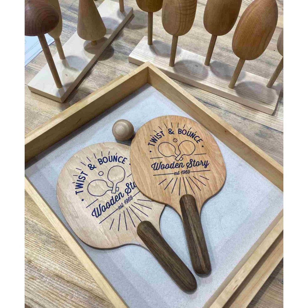 2. Wooden ping pong paddles with 'Twist & Bounce' logo in a wooden tray, surrounded by wooden toys on a table