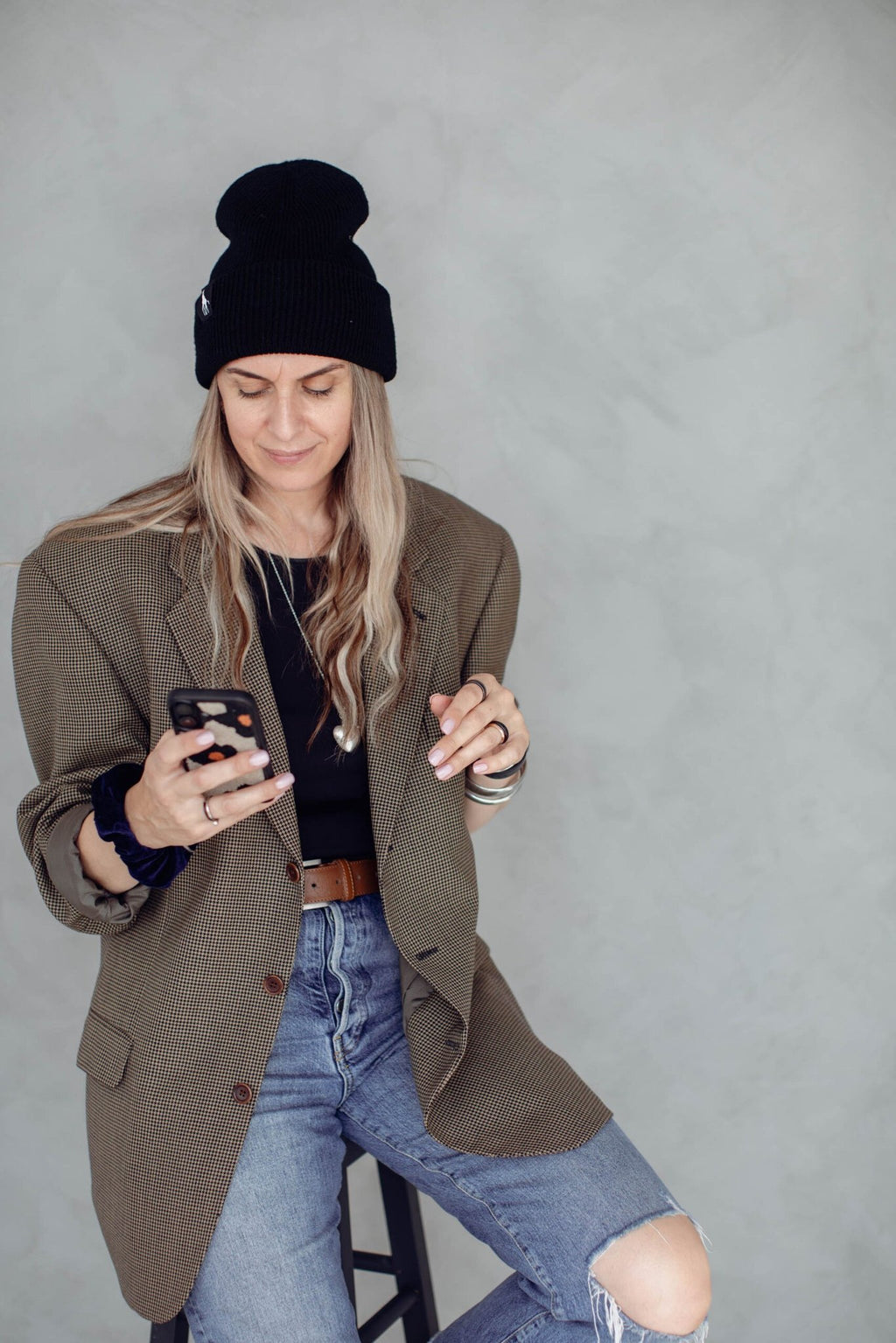 3. Woman wearing black beanie with giraffe label, seated and using smartphone, casual attire