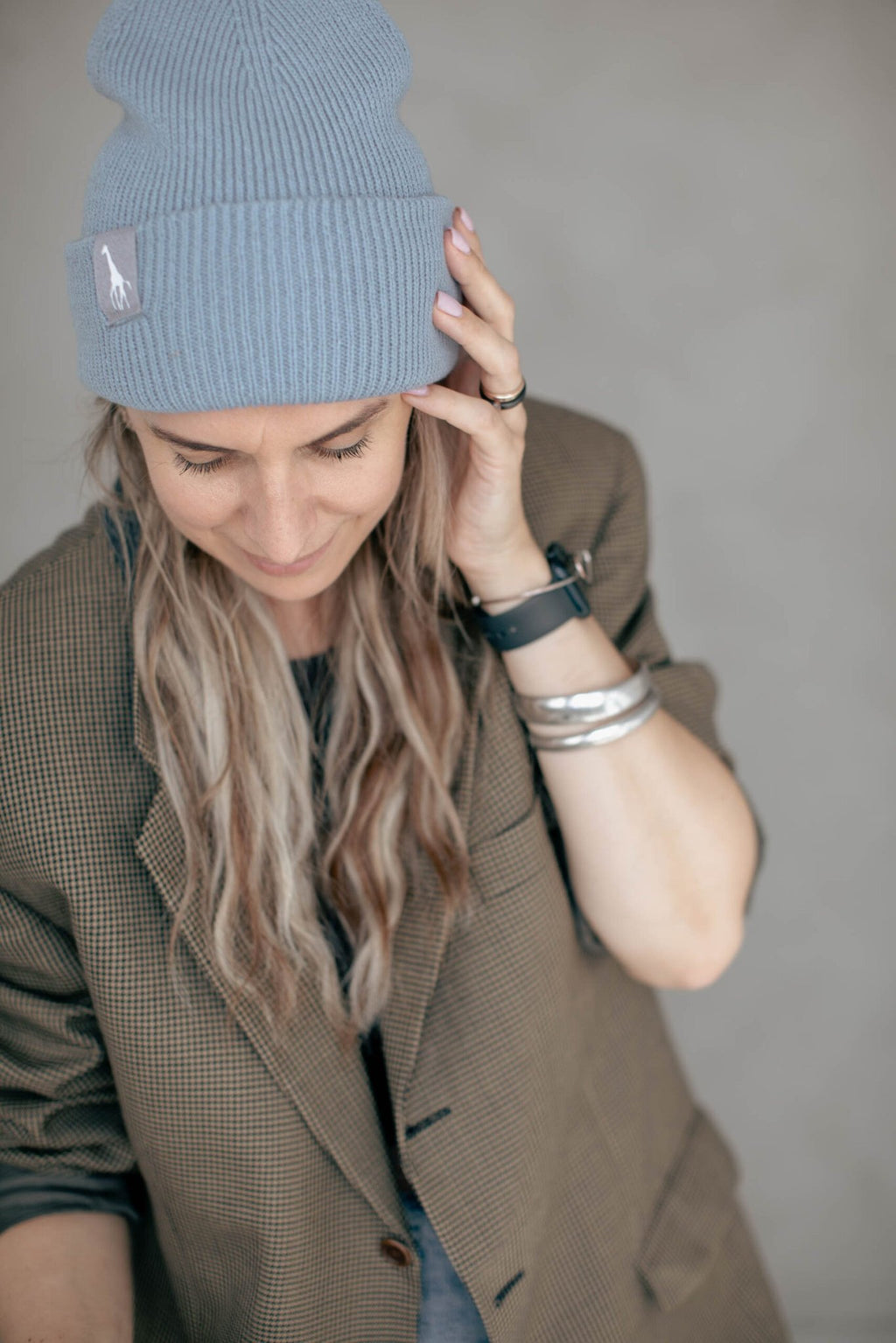 5. Woman in light blue beanie with giraffe label, smiling and touching hair, wearing casual blazer