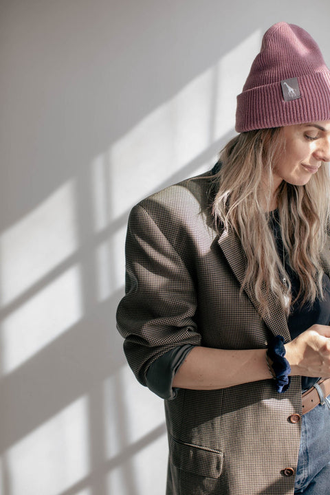 4. Woman in pink beanie with giraffe label, standing in sunlight, wearing casual blazer