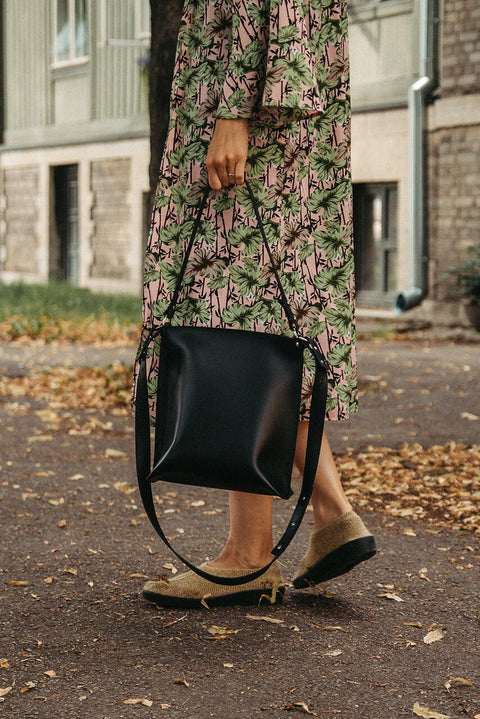 2. Close-up of black Stella Soomlais Escape Artist handbag held by woman in floral dress on leaf-strewn path