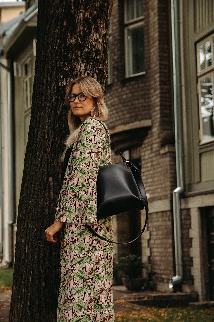 1. Woman wearing floral dress with black Stella Soomlais Escape Artist handbag leaning against tree in urban setting