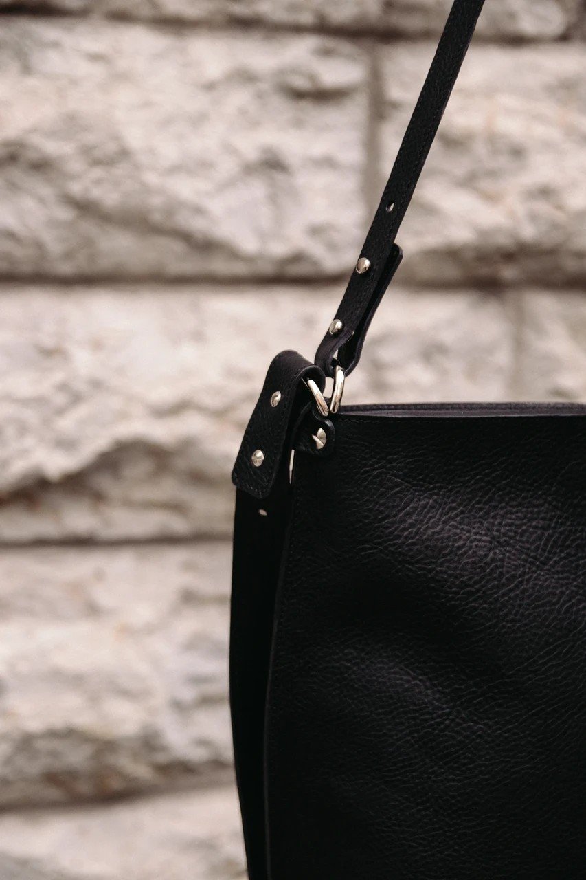 6. Close-up of black Stella Soomlais Escape Artist handbag strap and metal hardware against stone wall
