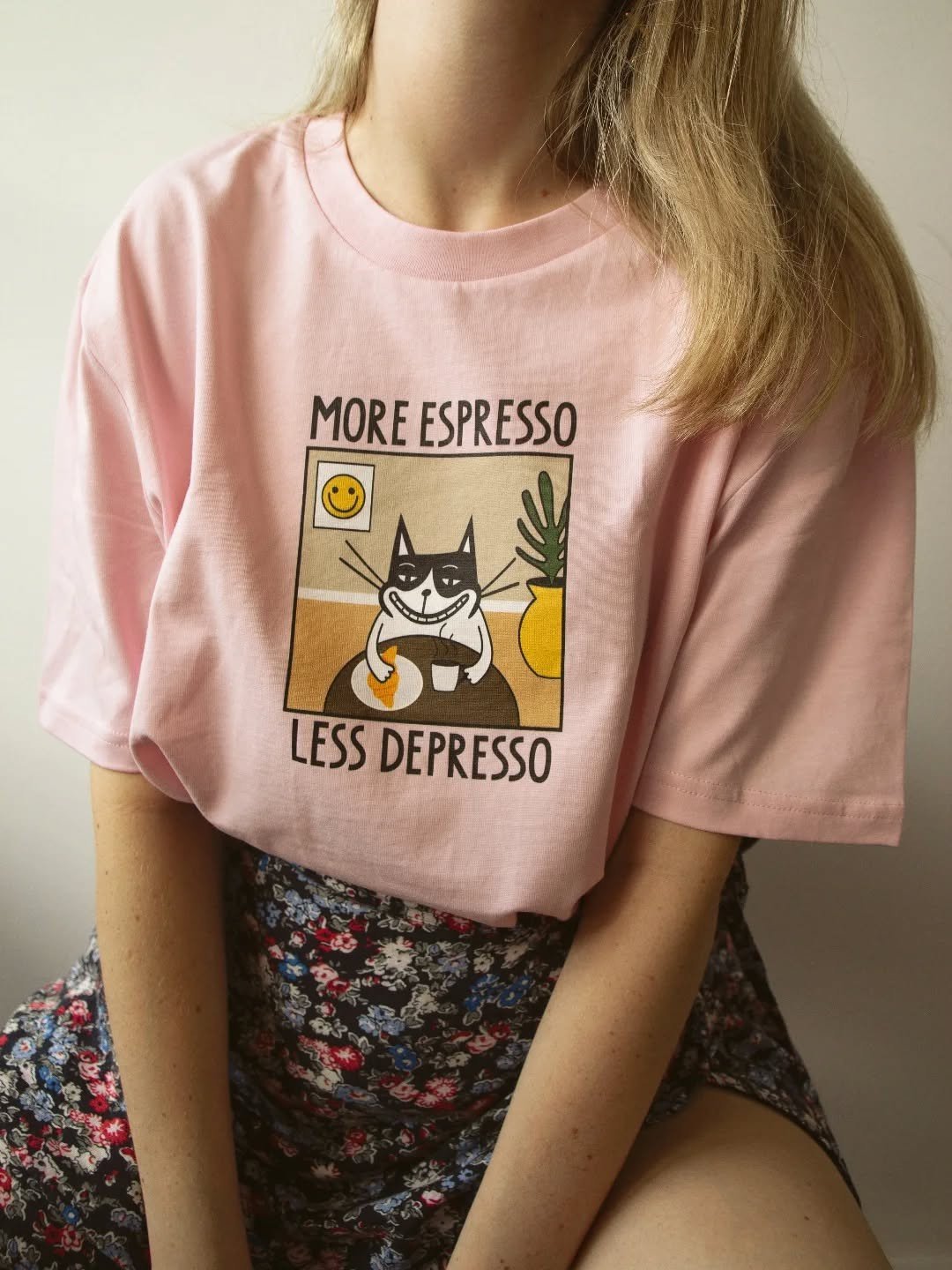 1. Woman wearing pink unisex T-shirt with 'More Espresso Less Depresso' print, sitting indoors
