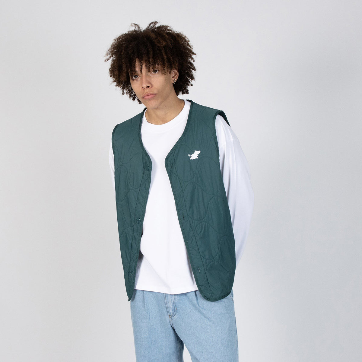 1. Male model wearing green unisex vest with Moomin logo over white shirt and jeans in studio setting