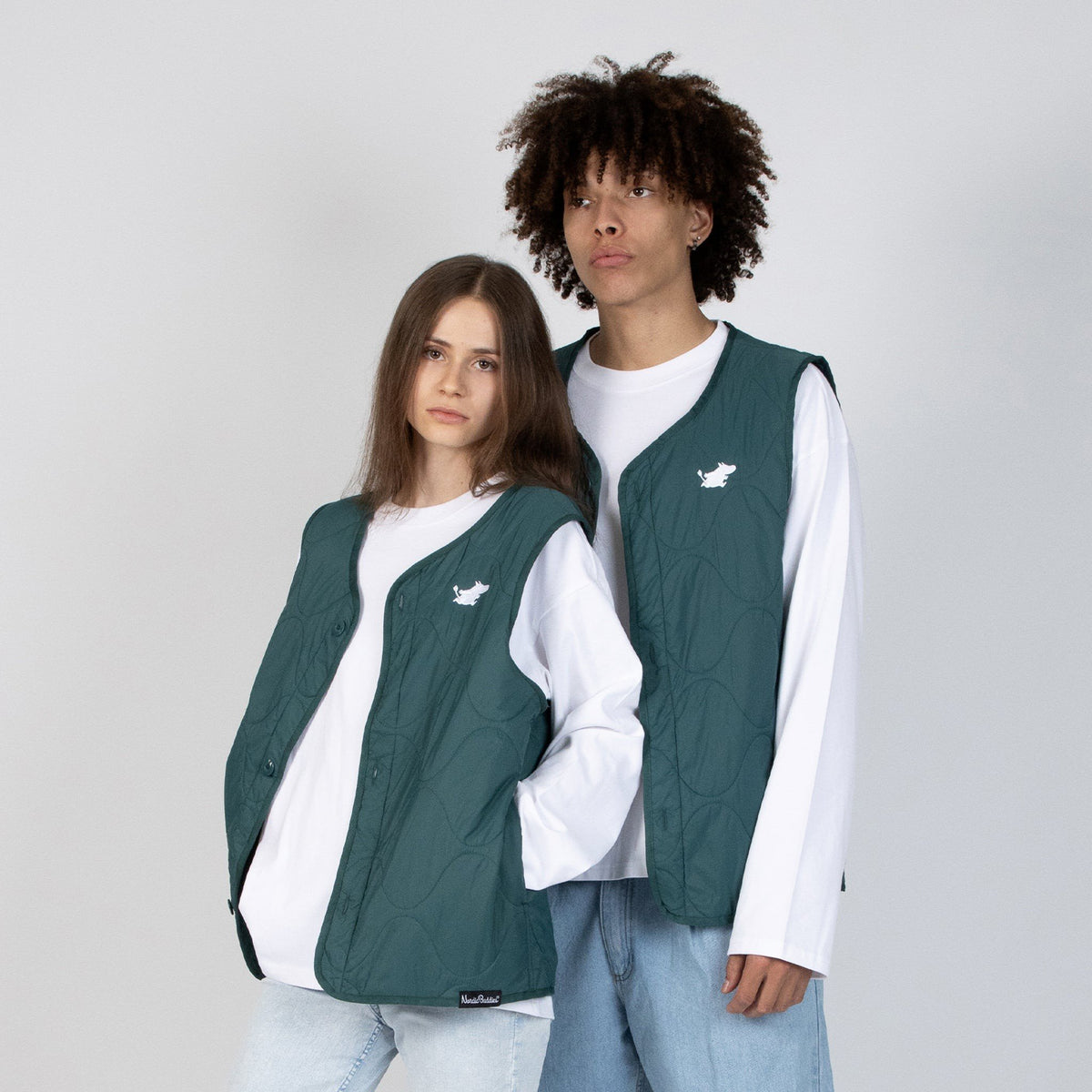 1. Male and female models wearing green unisex vests with Moomin logo over white shirts in studio setting