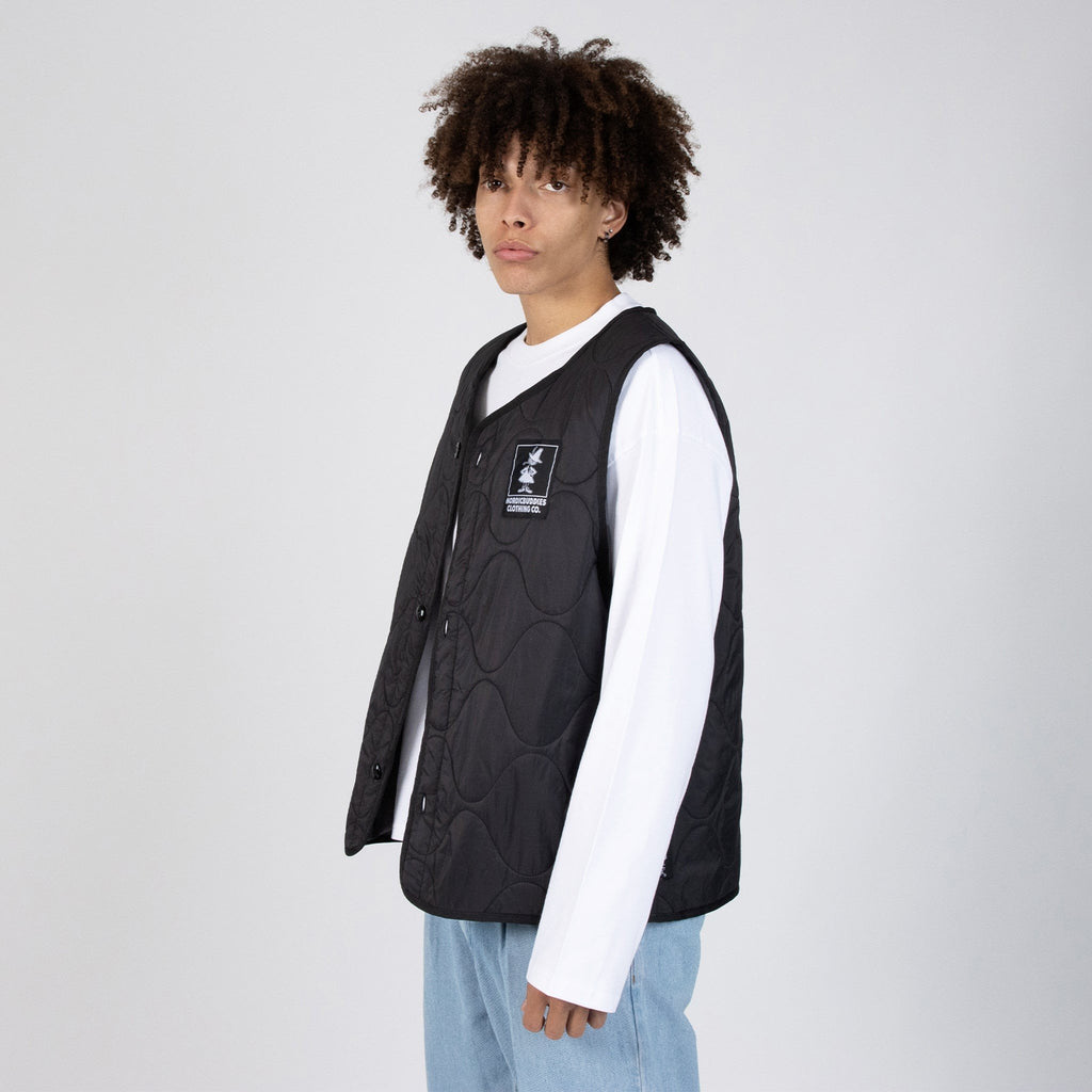 3. Male model wearing unisex black vest with NordicBuddies logo, paired with white shirt and jeans, side view in studio
