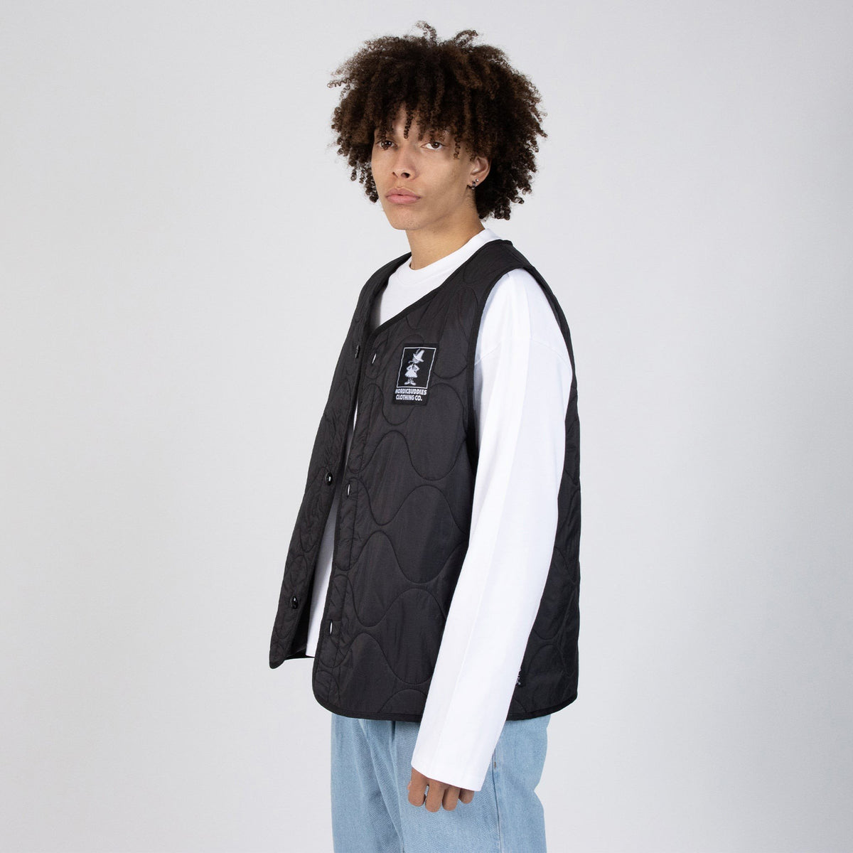 3. Male model wearing unisex black vest with NordicBuddies logo, paired with white shirt and jeans, side view in studio