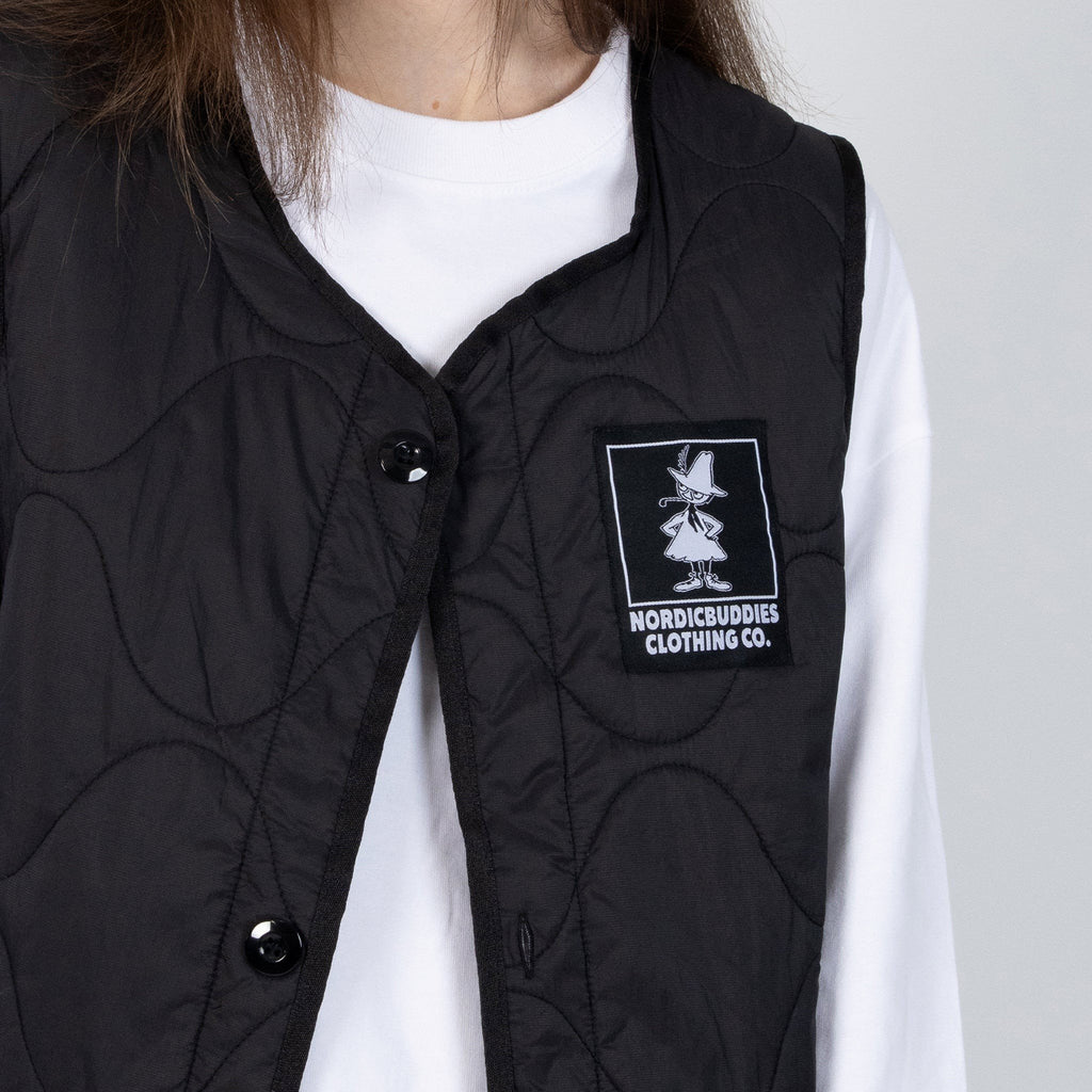 6. Close-up of NordicBuddies logo on black quilted vest worn by female model in white shirt