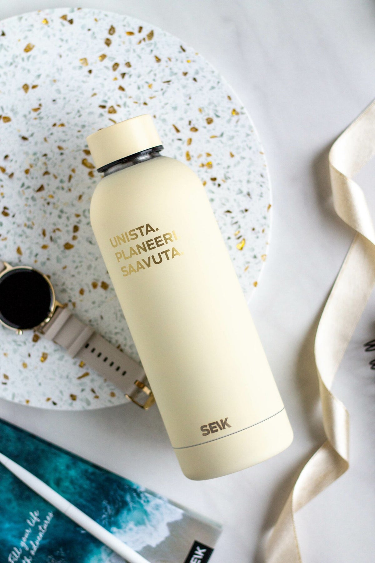 2. SEIK Unista thermos in beige, displayed on a terrazzo surface with a watch and ribbon