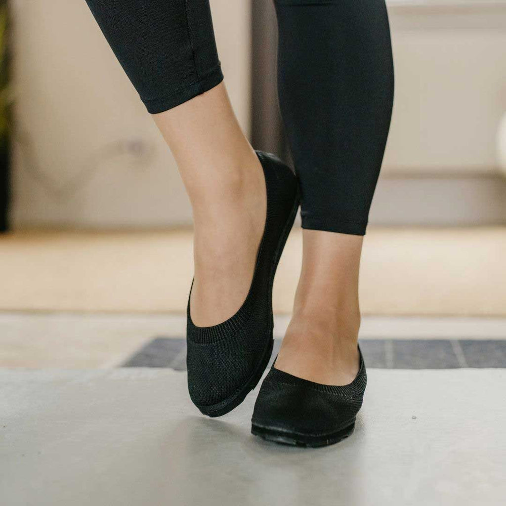6. Woman wearing black upcycled ballerina shoes by Kira Sustainable, shown walking indoors