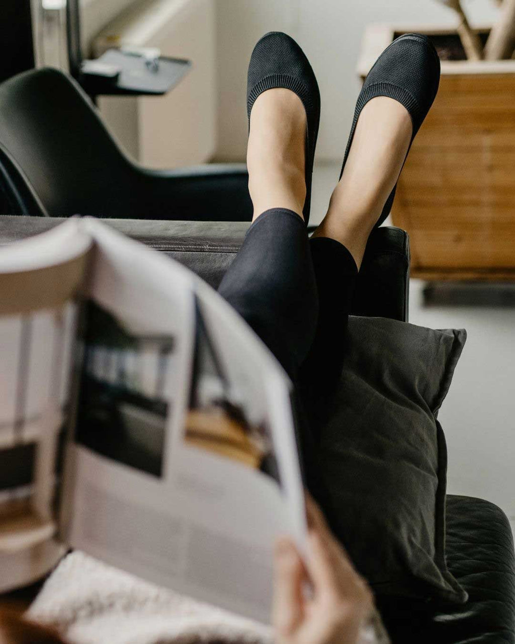 7. Woman relaxing on a couch wearing black upcycled ballerina shoes by Kira Sustainable, reading a magazine